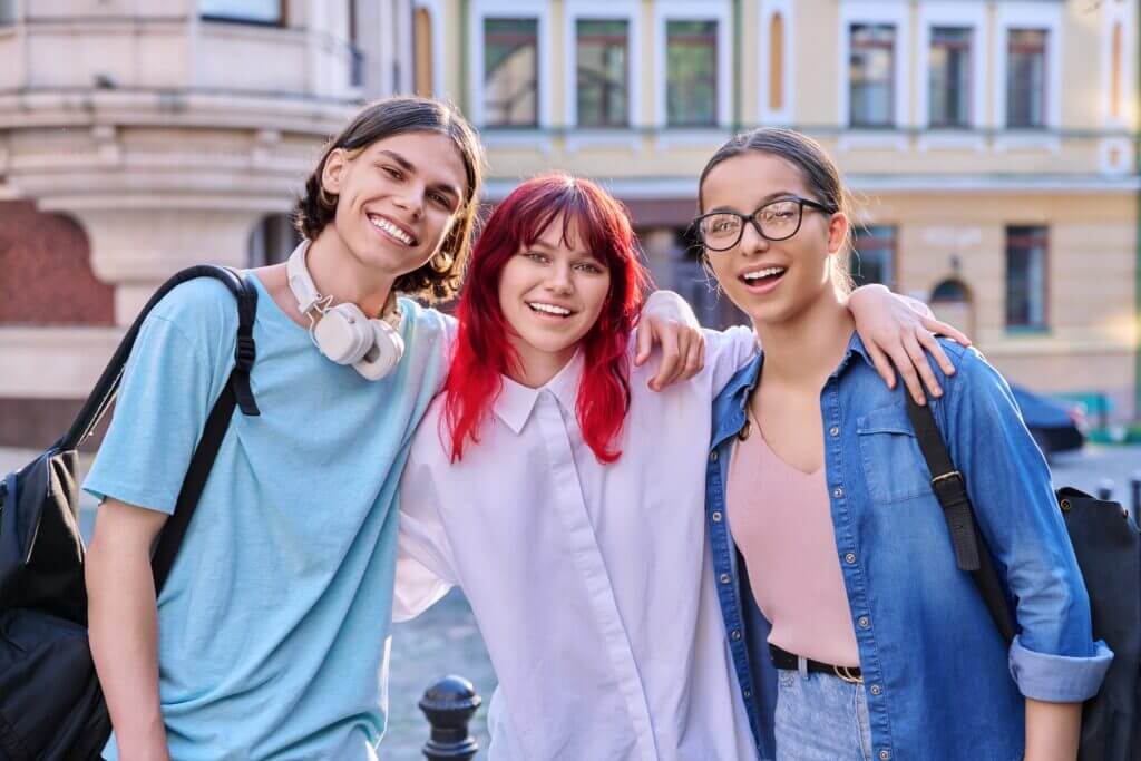 Happy smiling teenage friends hugging, looking at camera outdoor, on city street